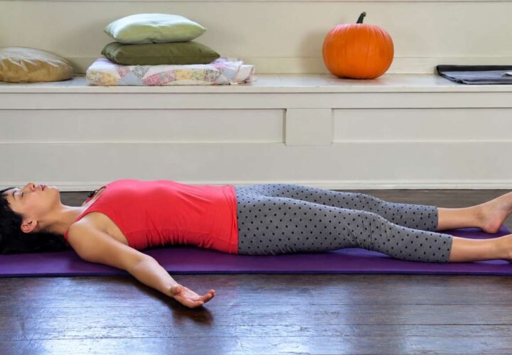 Woman resting on a yoga mat in Savasana pose.