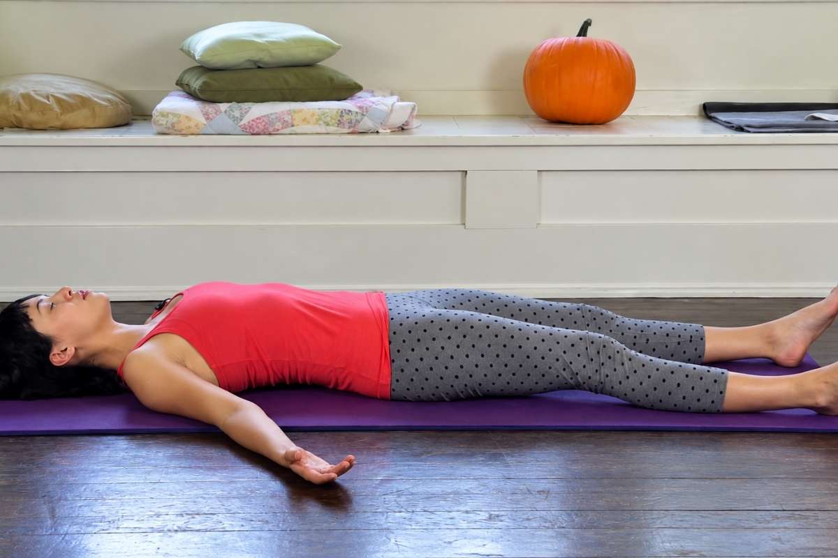Woman resting on a yoga mat in Savasana pose.