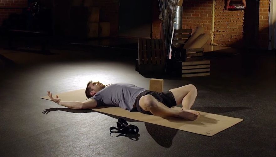 Man in Savasana pose on a yoga mat with arms extended.